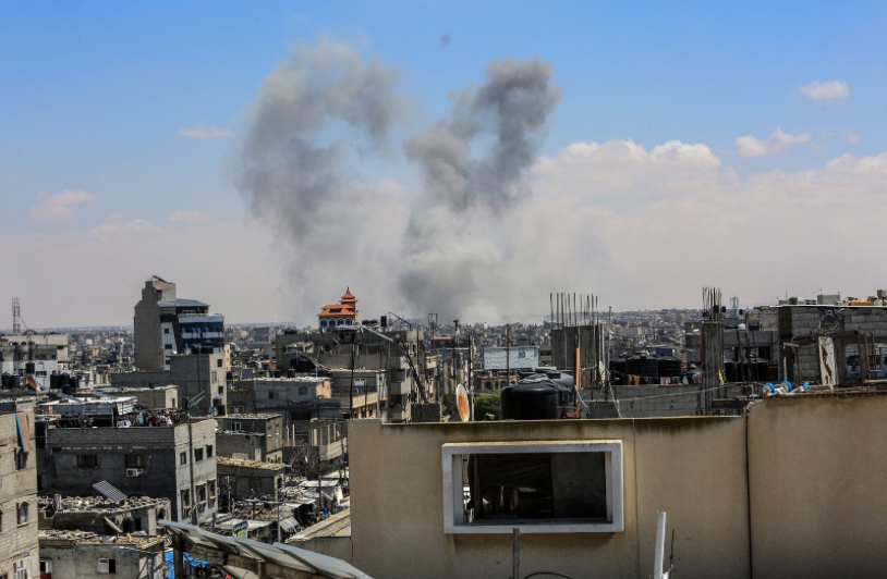 Smoke rises from buildings in a densely populated urban area, indicating an ongoing conflict, likely following airstrikes, as seen in the aftermath of violence between Israel and Hamas.